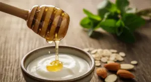 Miele che viene versato su una ciotola di yogurt con mandorle e fiocchi d'avena sullo sfondo